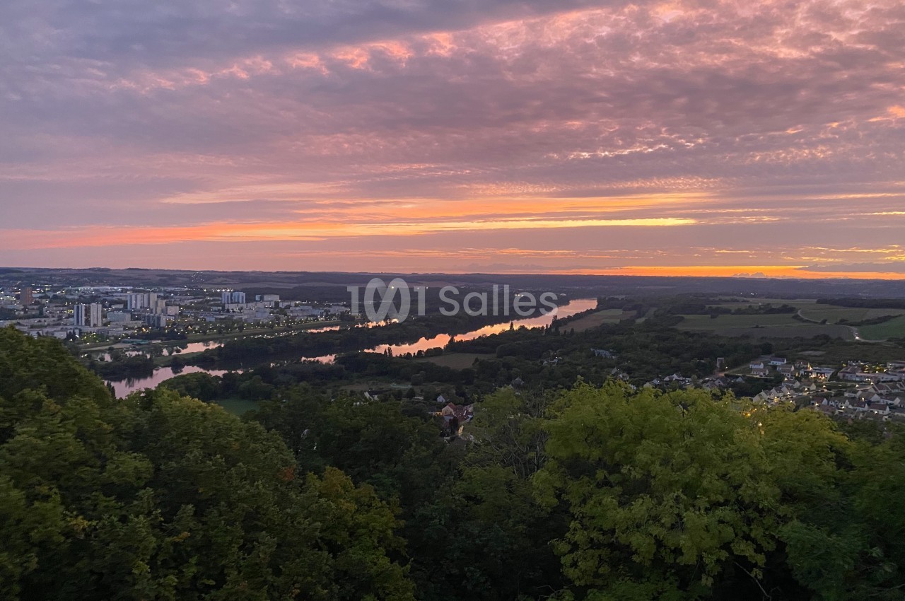 Vue panoramique d'une rivière serpentant entre des villes et des champs sous un ciel coloré au coucher du soleil.