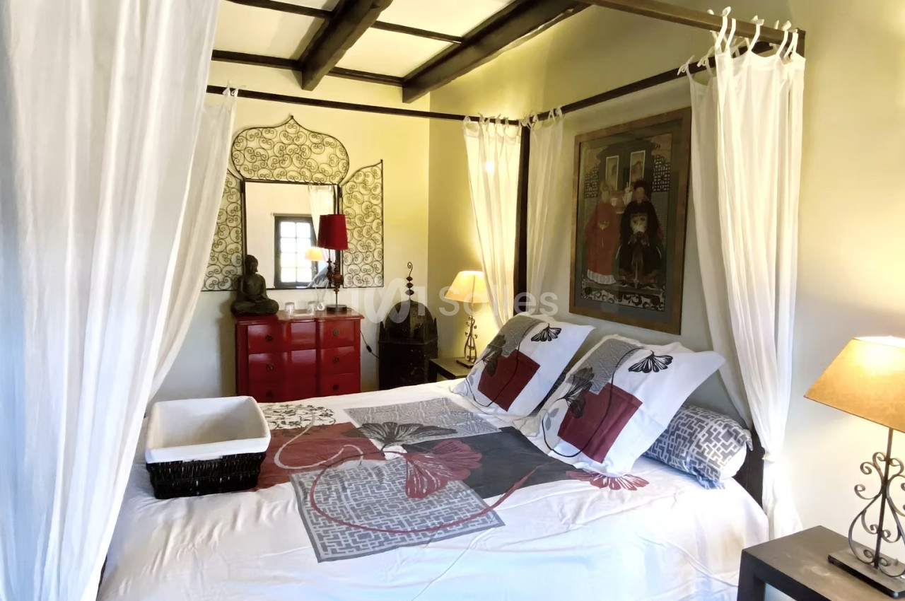 Chambre lumineuse avec lit à baldaquin, décorée de meubles rouges, lampes et tableaux muraux.