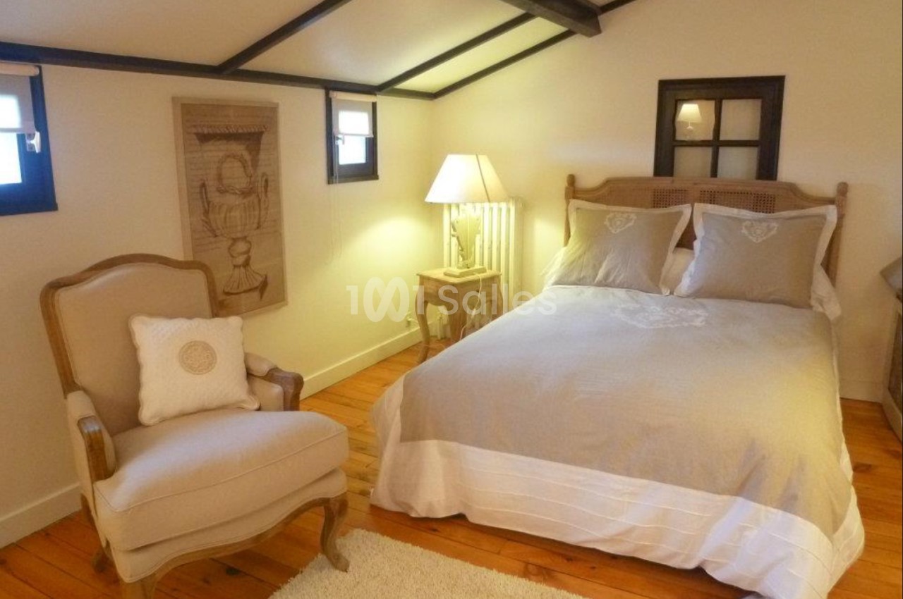 Chambre mansardée avec lit double, fauteuil, lampe de chevet et parquet en bois clair.