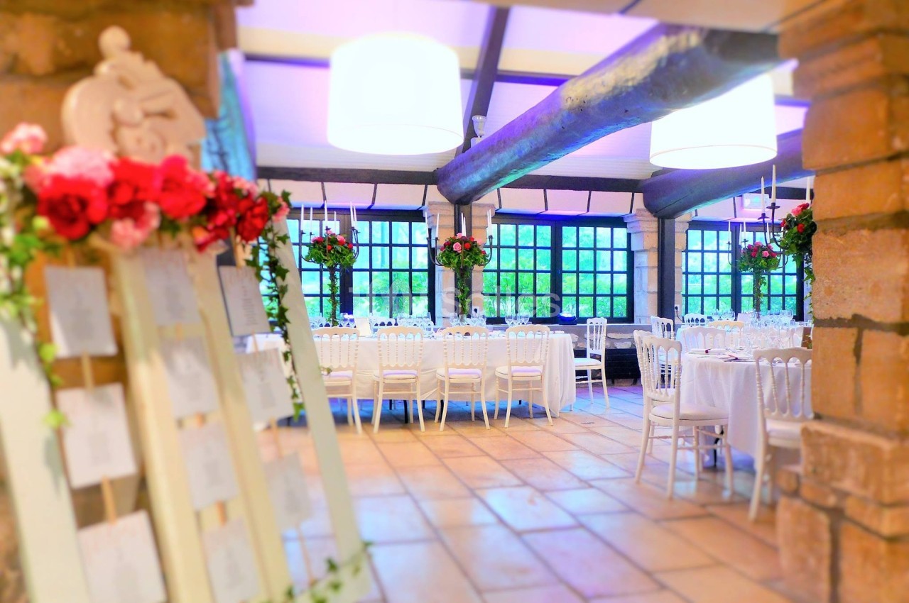 Salle de réception lumineuse avec tables décorées, chaises blanches et arrangements floraux rouges.