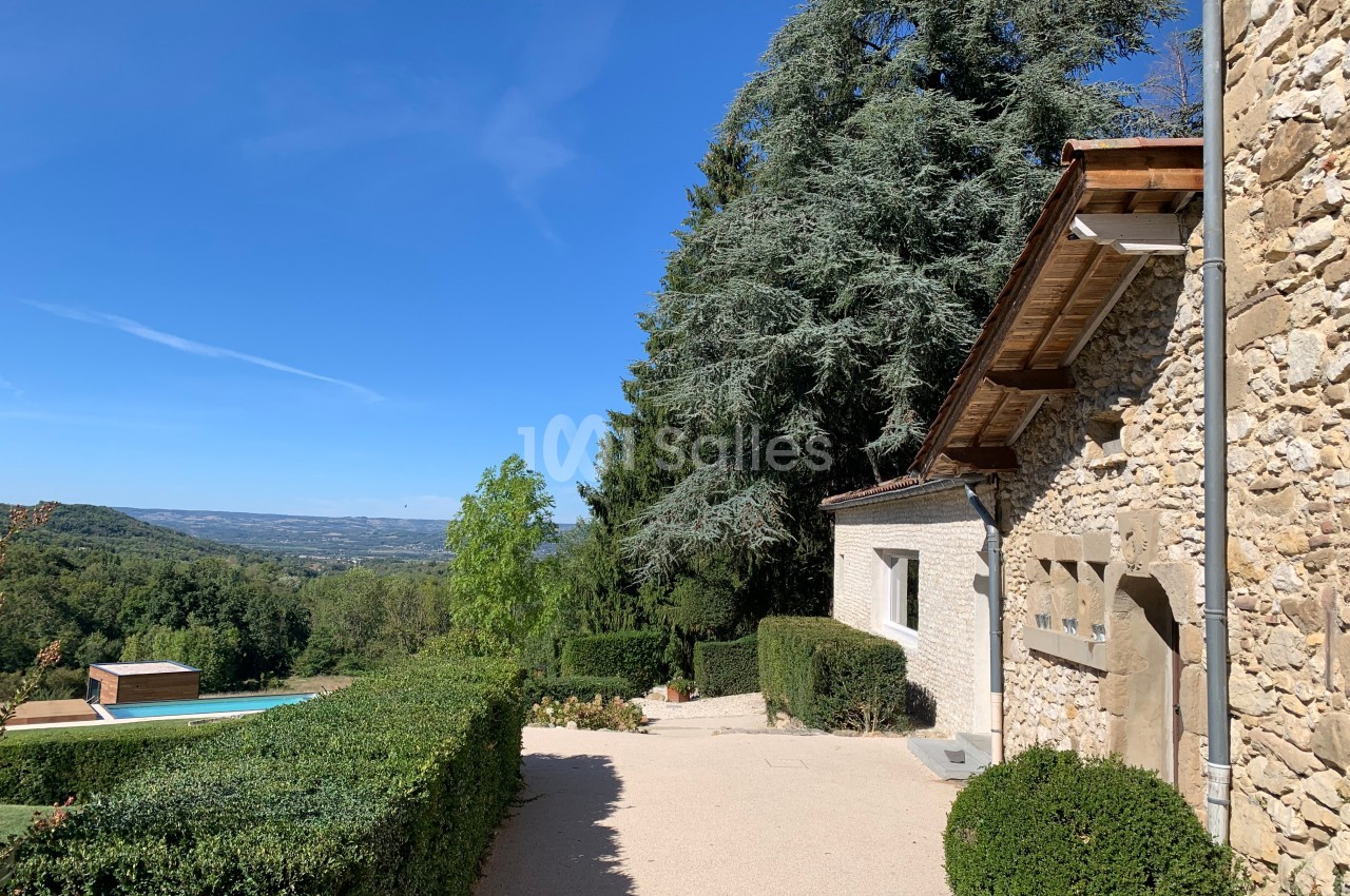 Maison en pierre avec jardin, piscine et vue dégagée sur une vallée sous un ciel bleu clair.