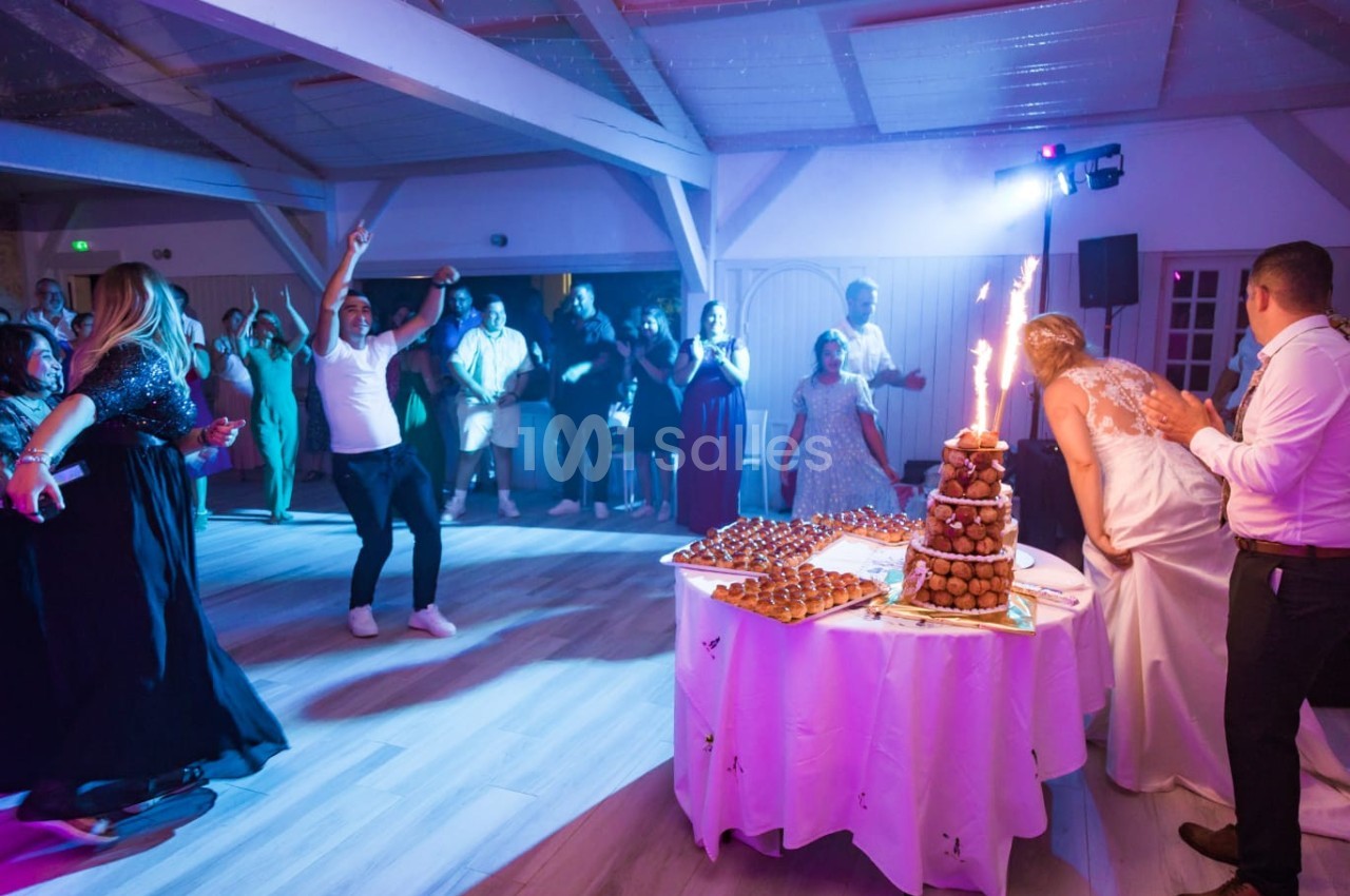Des invités dansent autour d'une pièce montée éclairée par des cierges magiques lors d'une fête en salle.