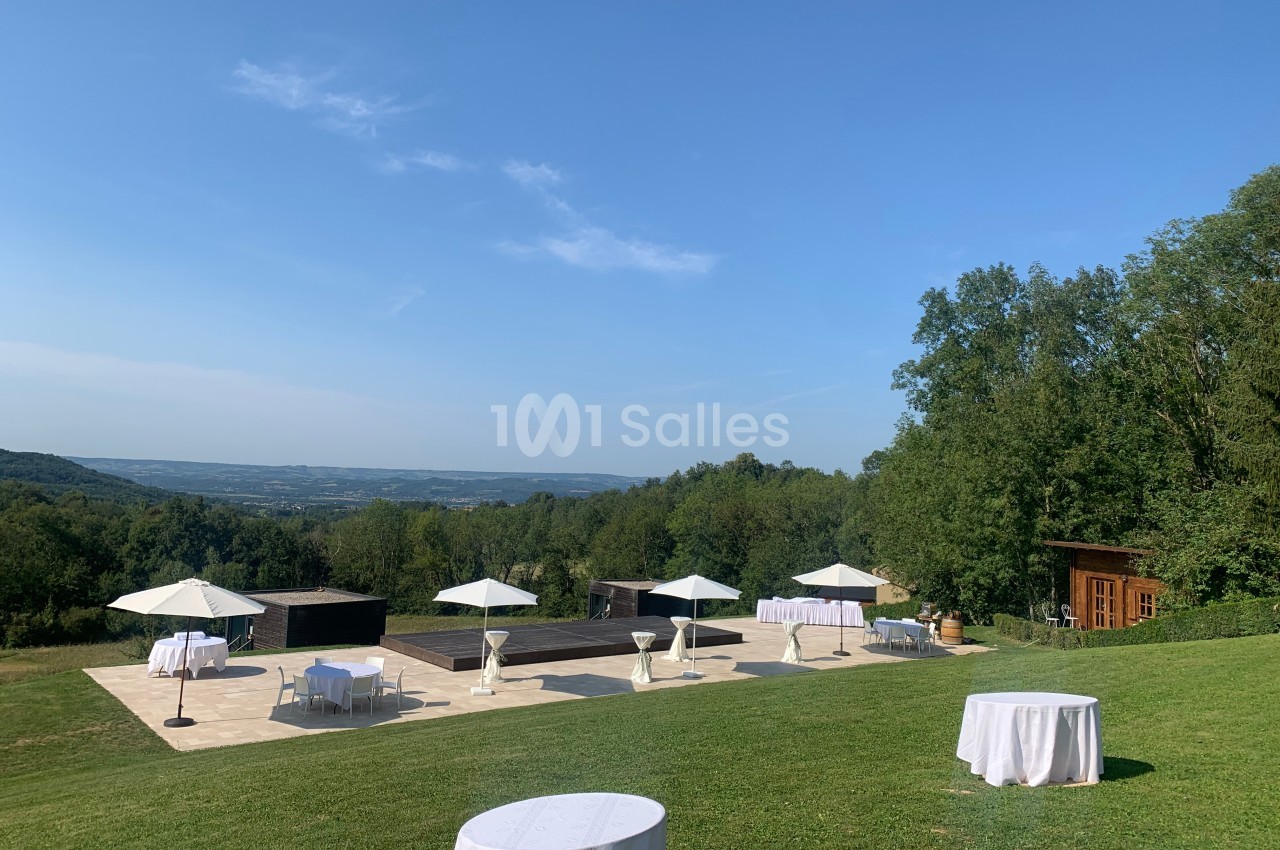 Terrasse extérieure avec tables et parasols blancs, entourée de verdure et offrant une vue dégagée sur la vallée.