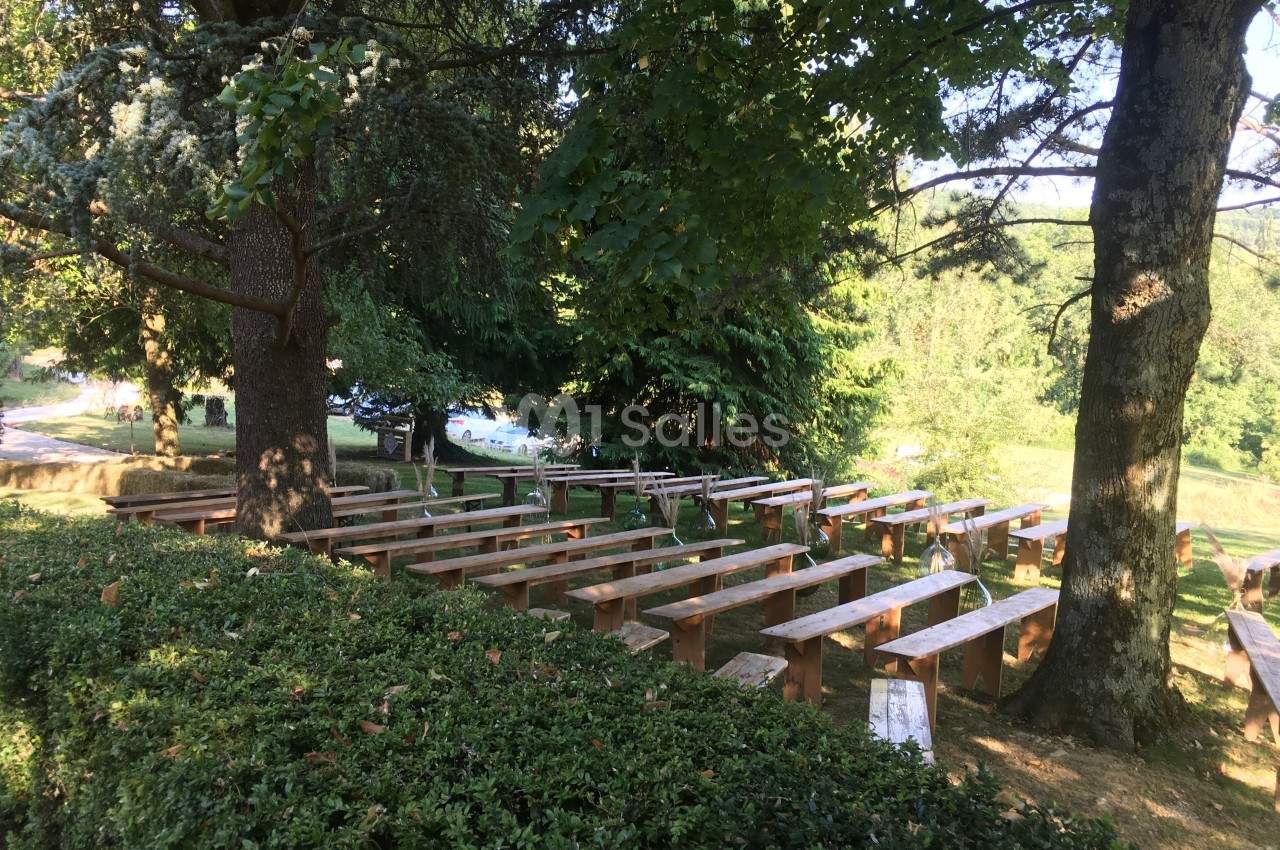 Bancs en bois disposés en rangées sous des arbres dans un espace extérieur verdoyant.