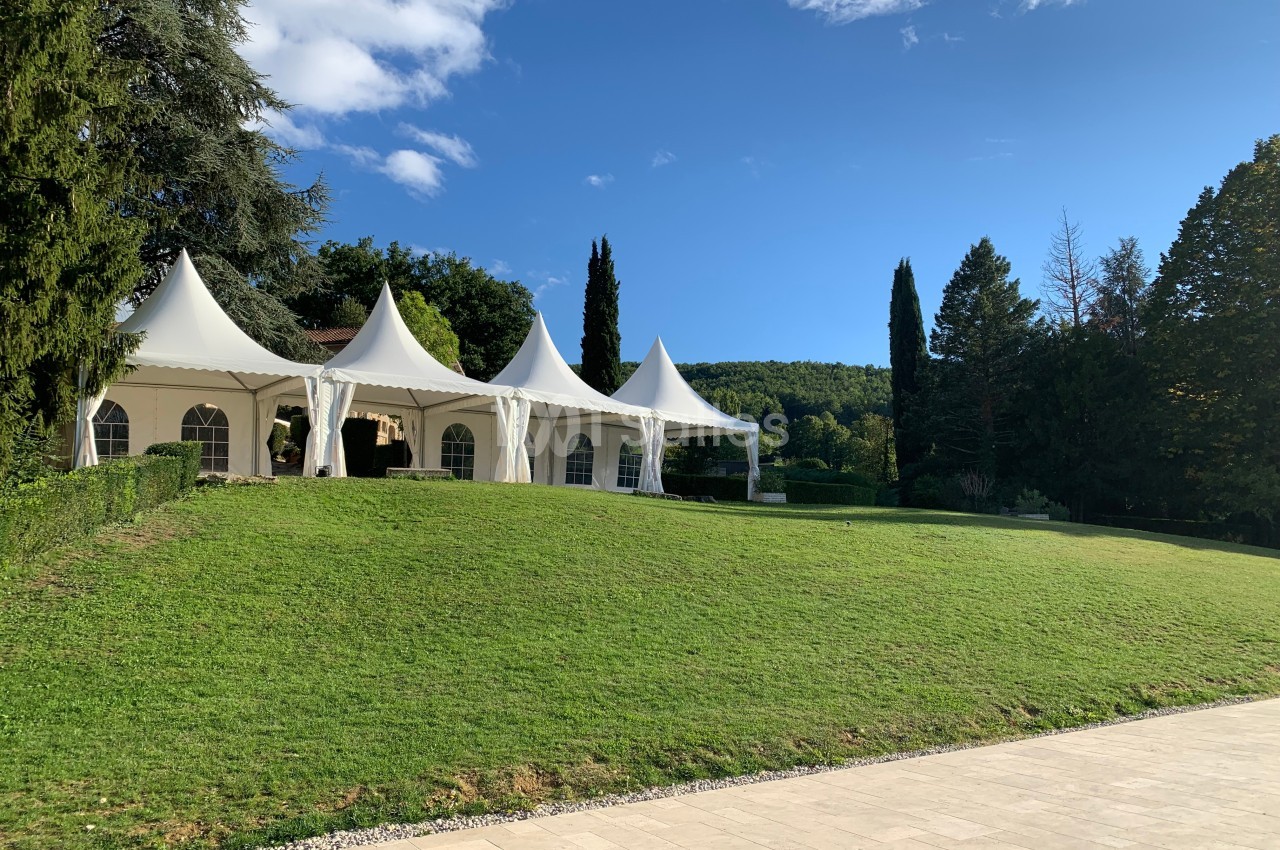 Tentes blanches installées sur une pelouse verdoyante, entourées d'arbres et sous un ciel bleu dégagé.