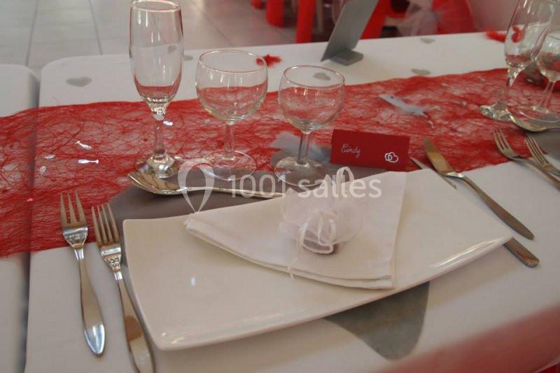 Table dressée avec une nappe blanche, chemin de table rouge, vaisselle élégante et serviette pliée avec un ruban.