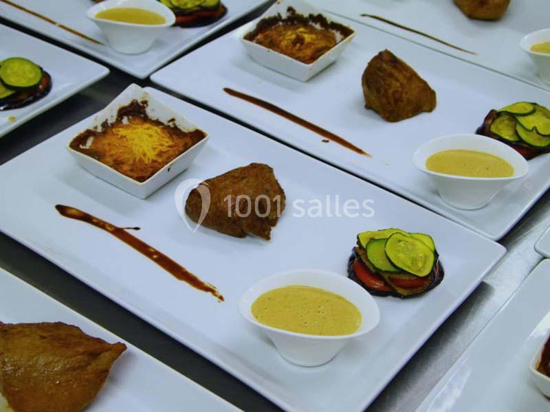 Assiettes gastronomiques avec viande, gratin, légumes et sauce disposés de manière soignée sur des plateaux blancs.