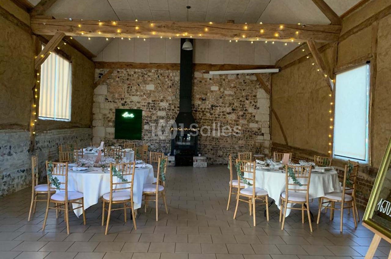 Salle de réception rustique avec murs en pierre, tables dressées et guirlandes lumineuses suspendues.