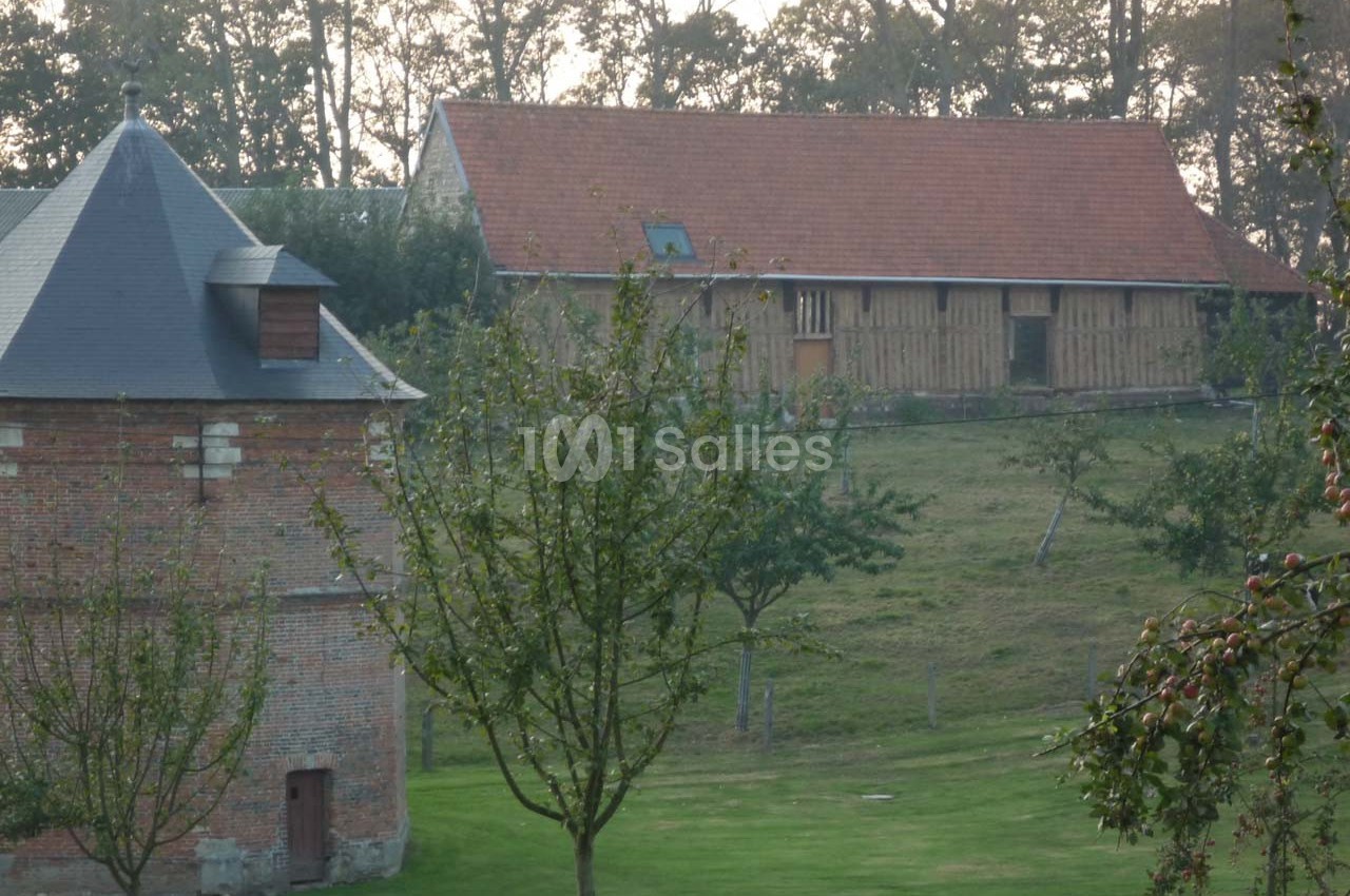 Bâtiments en briques et en bois dans un paysage rural avec arbres et pelouse au premier plan.