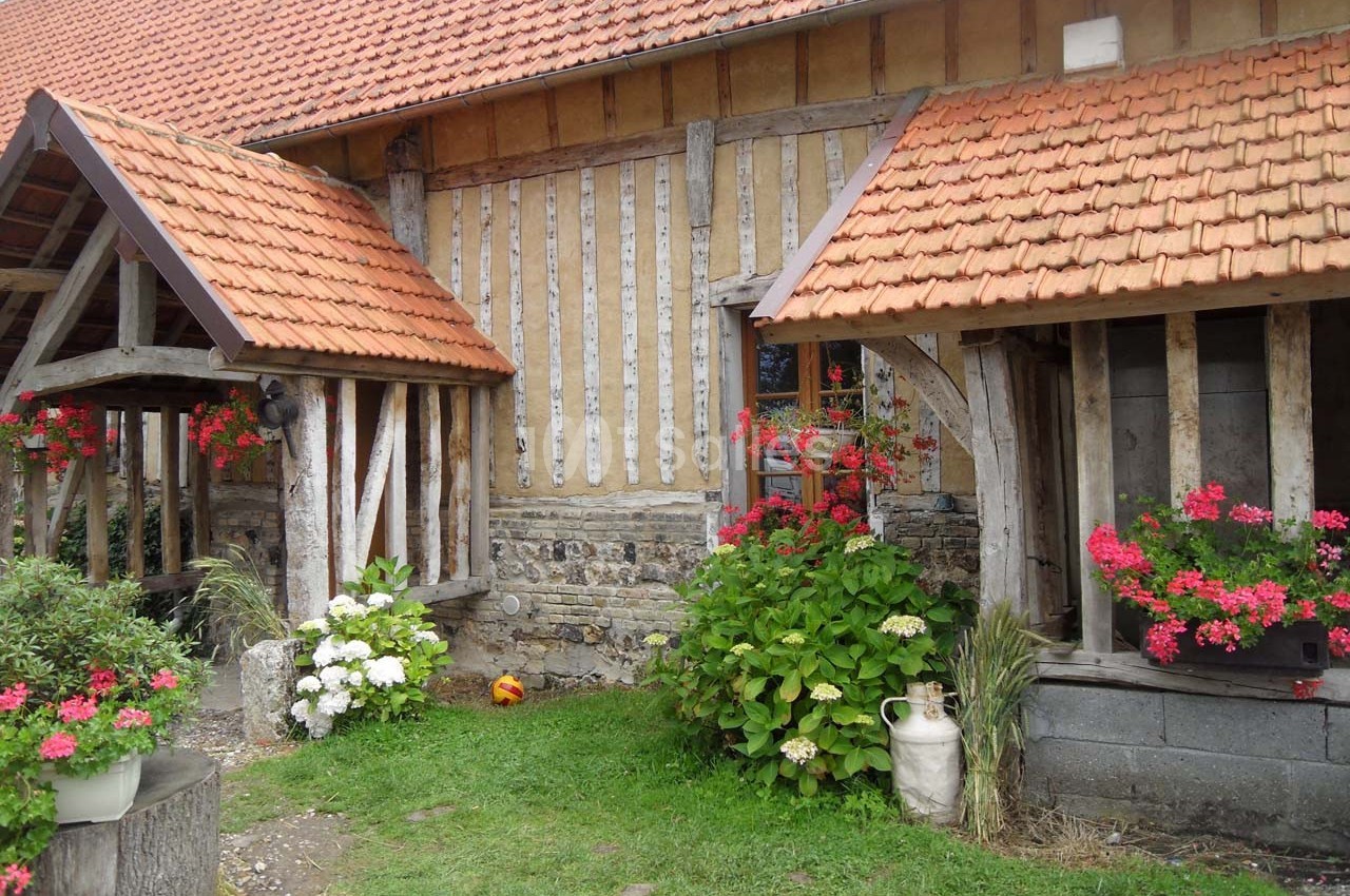 Maison à colombages avec toit en tuiles, entourée de fleurs colorées et d'un jardin verdoyant.