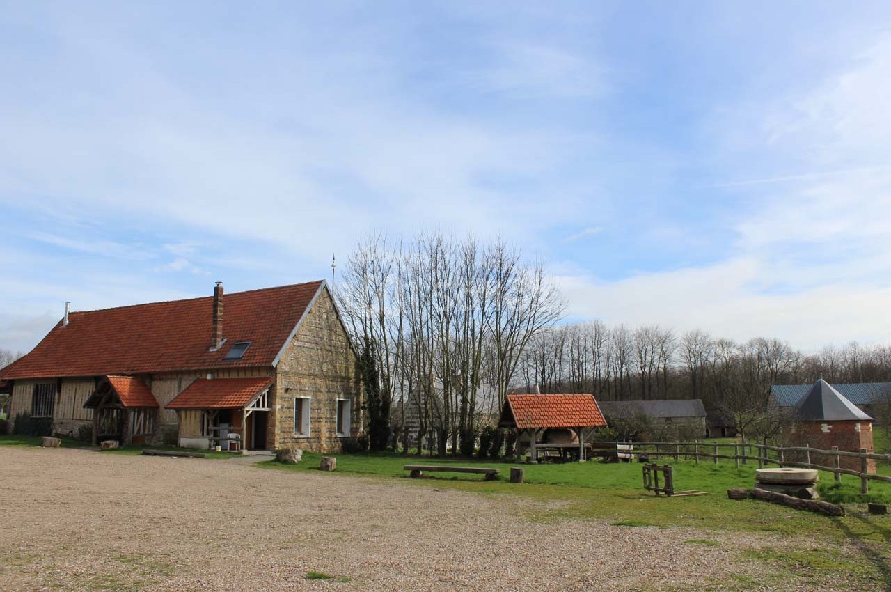 Bâtiments en pierre avec toits rouges dans un paysage rural, entourés d'arbres et d'une cour dégagée.
