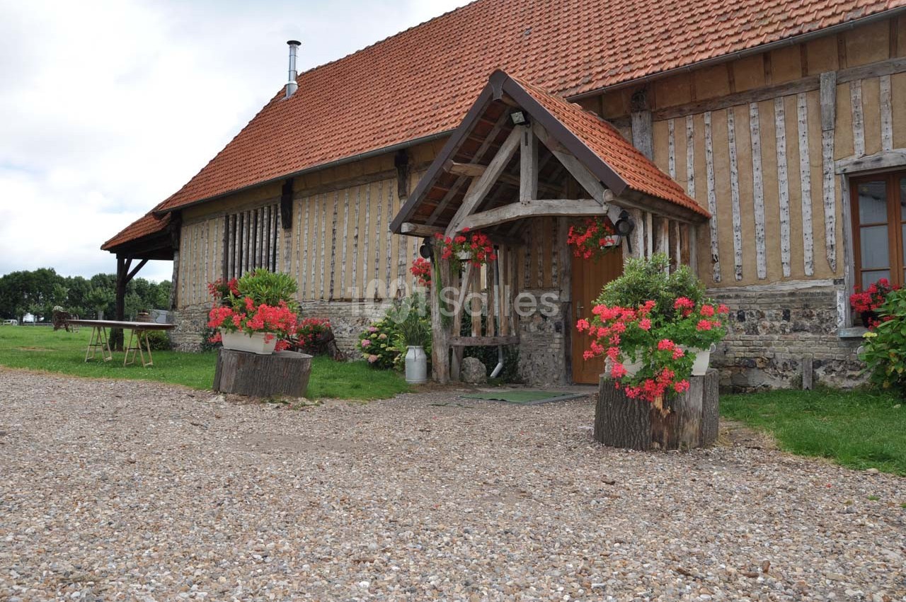Façade d'une maison à colombages avec toit en tuiles, jardinières fleuries et entrée abritée par une structure en bois.