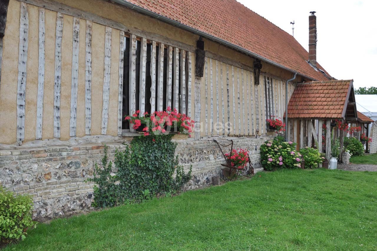 Façade d'une maison à colombages avec des fleurs en jardinières, un toit en tuiles et un jardin verdoyant.