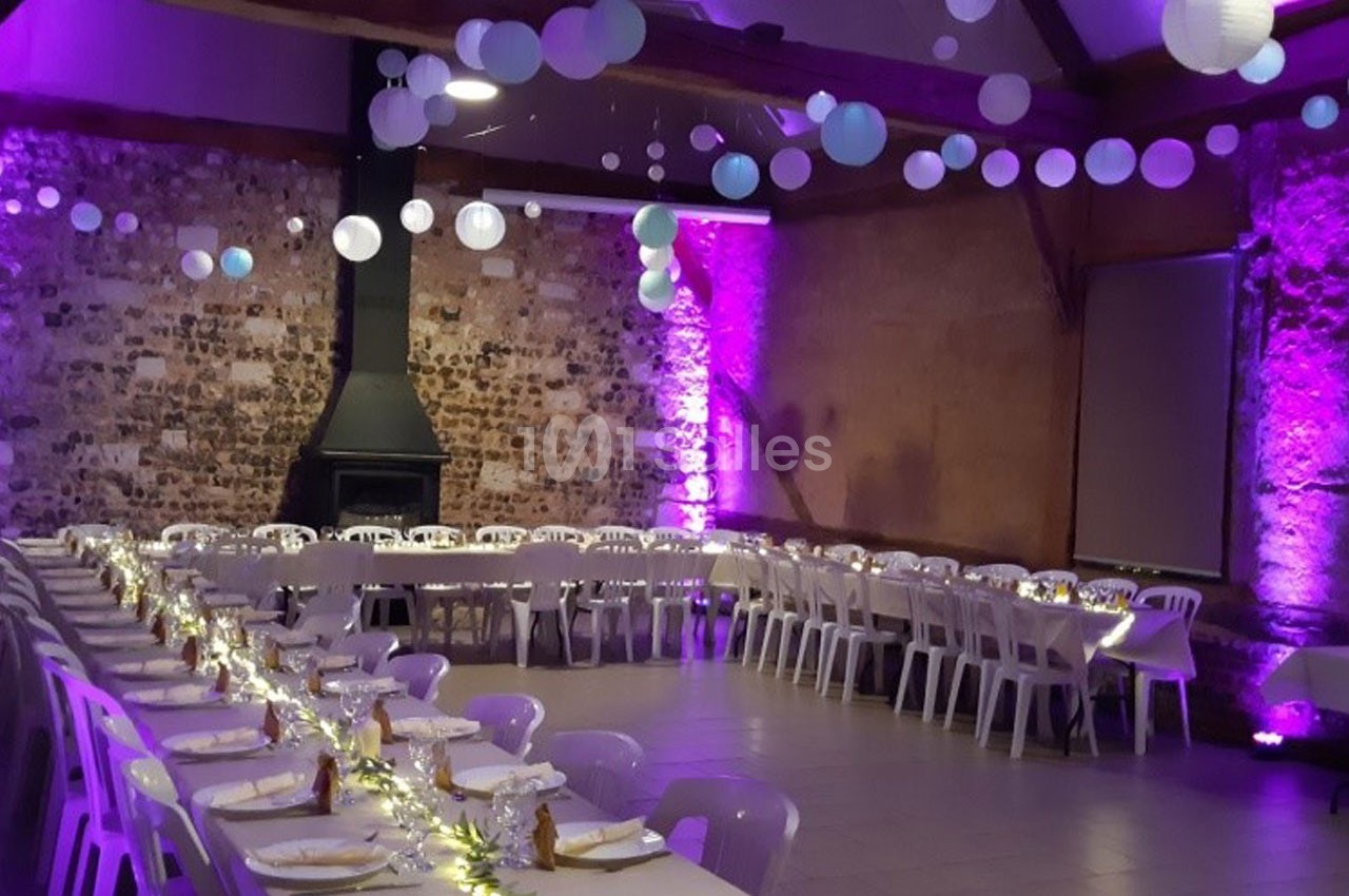 Salle de réception décorée avec des guirlandes lumineuses, des lanternes suspendues et des tables alignées pour un événement.