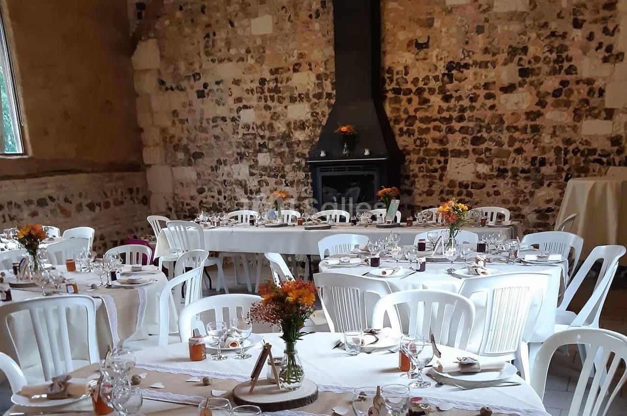 Salle décorée pour un événement avec des tables dressées, des chaises blanches et des fleurs en centre de table.
