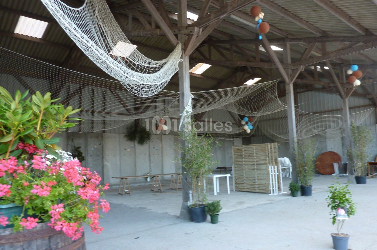 Intérieur d'une grange décorée avec des filets suspendus, des plantes en pot et des tables en bois.