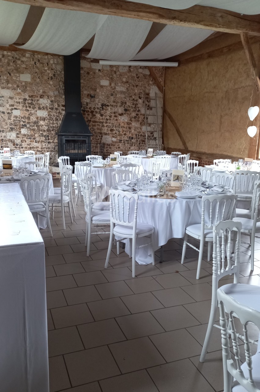Salle de réception avec murs en pierre, tables rondes dressées de nappes blanches et chaises assorties.