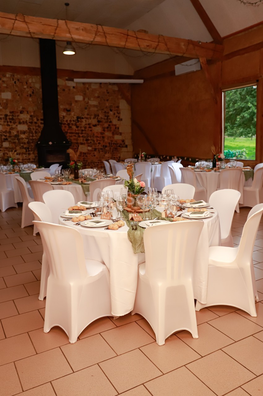 Salle de réception avec tables rondes dressées, nappes blanches, chaises assorties et décoration florale.