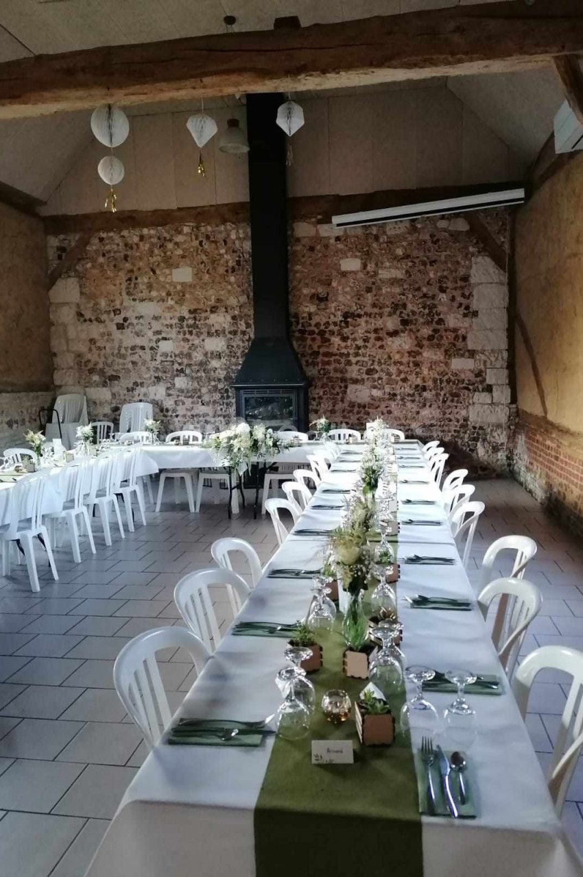Salle rustique avec murs en pierre, tables dressées avec nappes blanches, chemins de table verts et décoration florale.