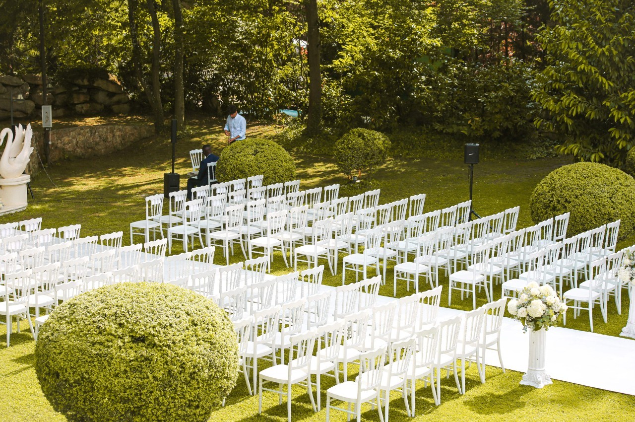 Chaises blanches alignées en extérieur pour une cérémonie, entourées de buissons taillés et d'arbres.