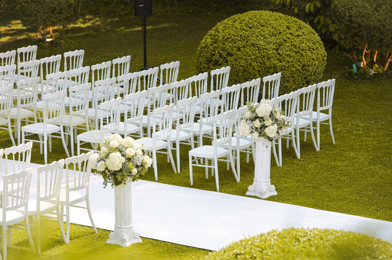 Chaises blanches alignées en extérieur, disposées devant une allée blanche bordée de compositions florales.