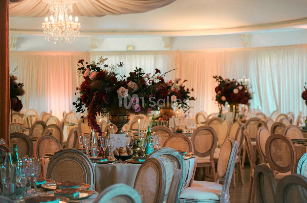 Salle de réception élégante avec tables décorées de fleurs et chaises en bois clair sous un éclairage chaleureux.