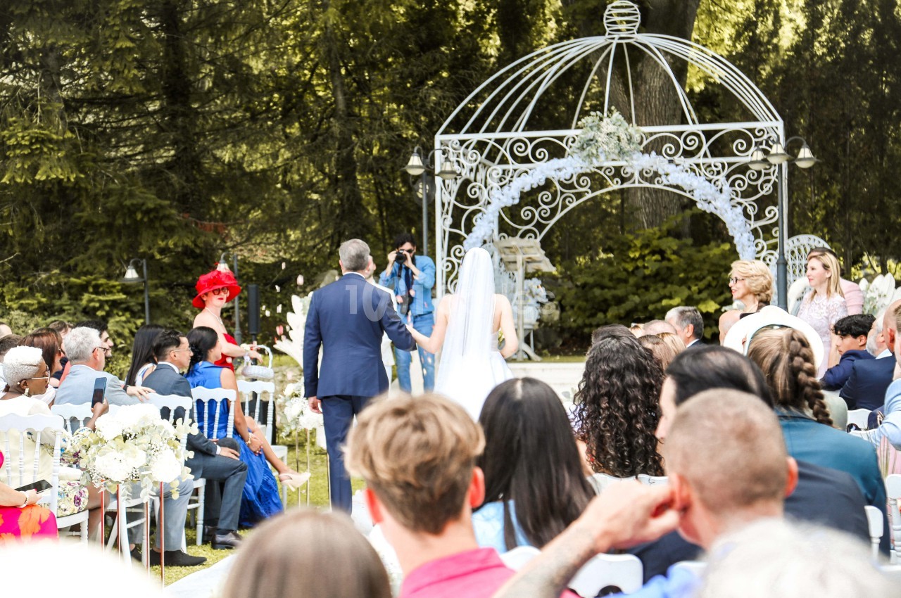 Cérémonie de mariage en plein air avec des invités assis, un couple avançant vers une arche décorée.
