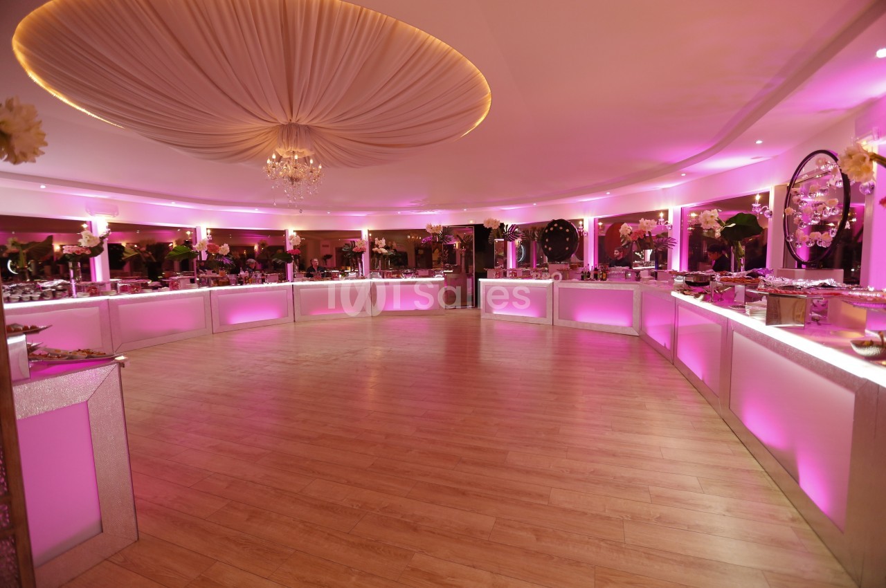 Salle de réception circulaire avec éclairage rose, plafond drapé et tables de buffet alignées le long des murs.