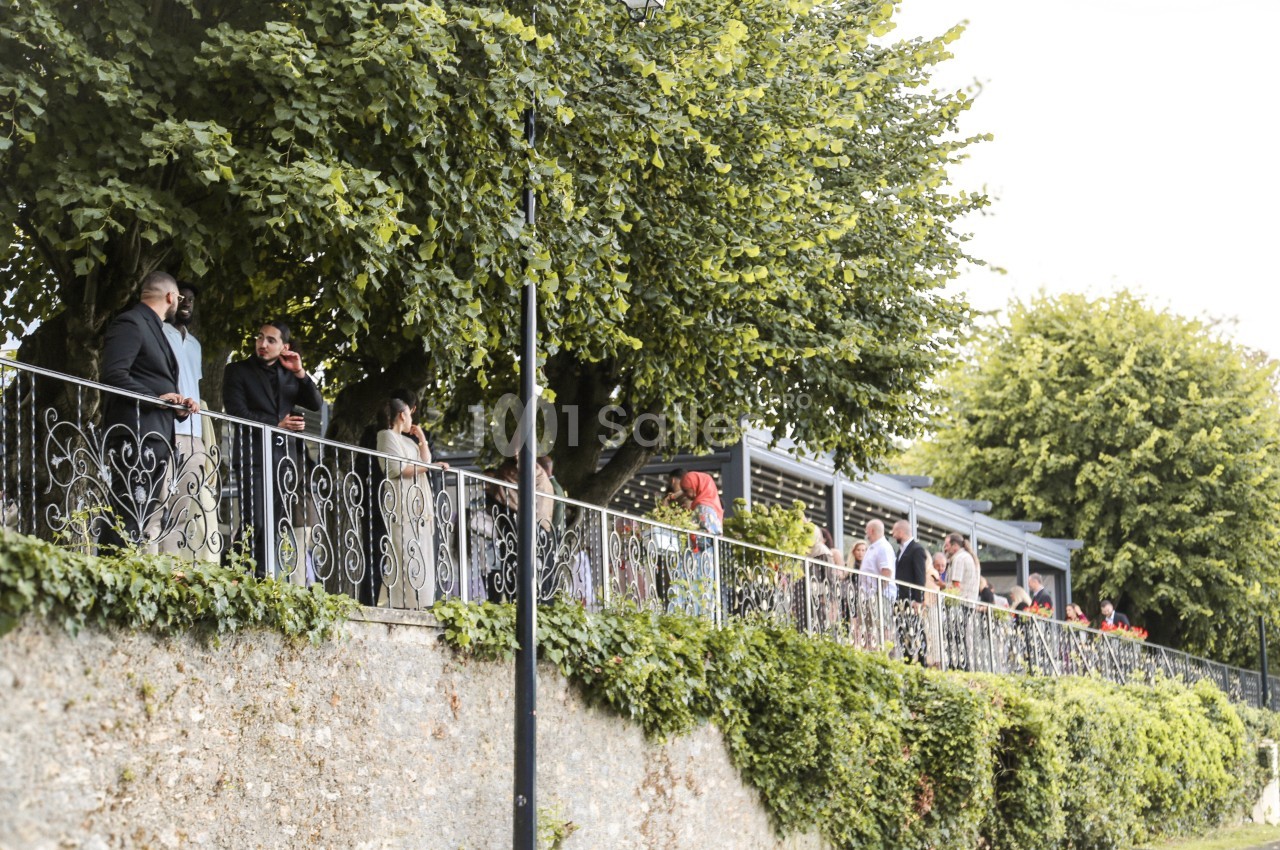 Des personnes discutent et se promènent le long d'une balustrade entourée de verdure et d'arbres.