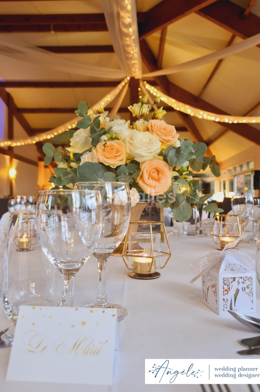 Table de mariage décorée avec des roses, des bougies dorées et des cadeaux d'invités, sous un plafond illuminé.