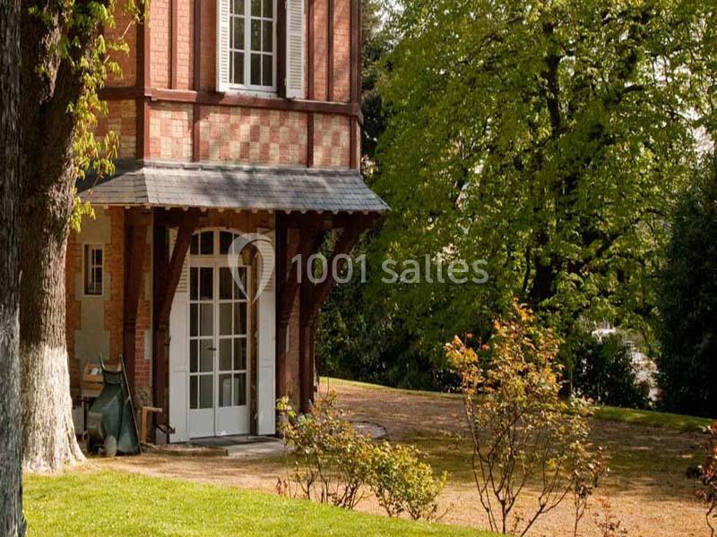 Façade d'une maison en briques avec une porte vitrée, entourée d'arbres et d'un jardin ensoleillé.