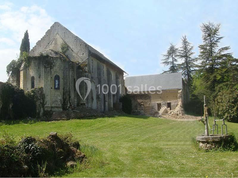 Vue d'une ancienne église en pierre entourée de verdure, avec un puits au premier plan et des bâtiments annexes.