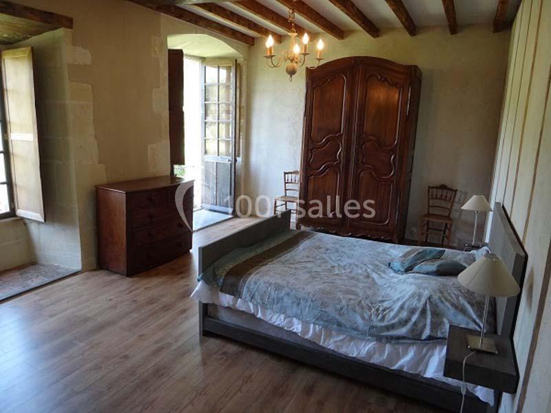Chambre avec lit double, armoire en bois, commode, parquet et lumière naturelle entrant par une porte-fenêtre.