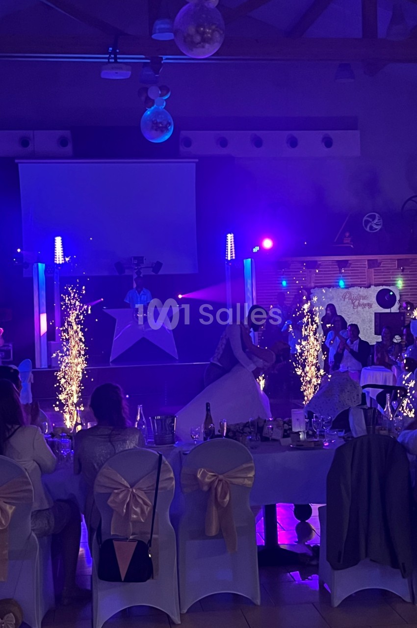 Un couple danse au centre d'une salle de réception éclairée par des lumières colorées et des étincelles.