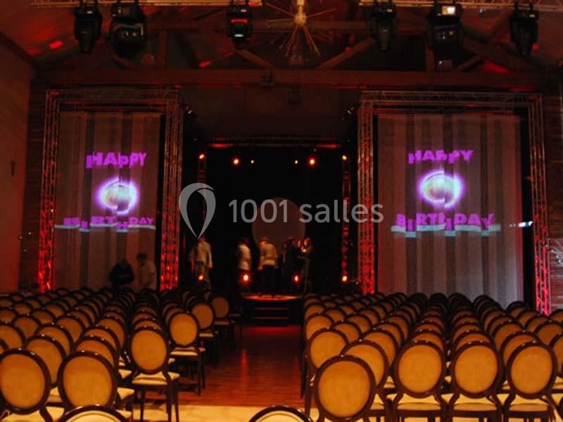 Salle de spectacle avec rangées de chaises vides, scène éclairée et écrans affichant ’Happy Birthday’.