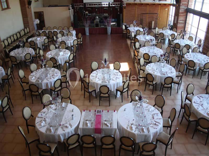 Salle de réception avec tables rondes dressées pour un événement, entourées de chaises et décorées de nappes blanches.