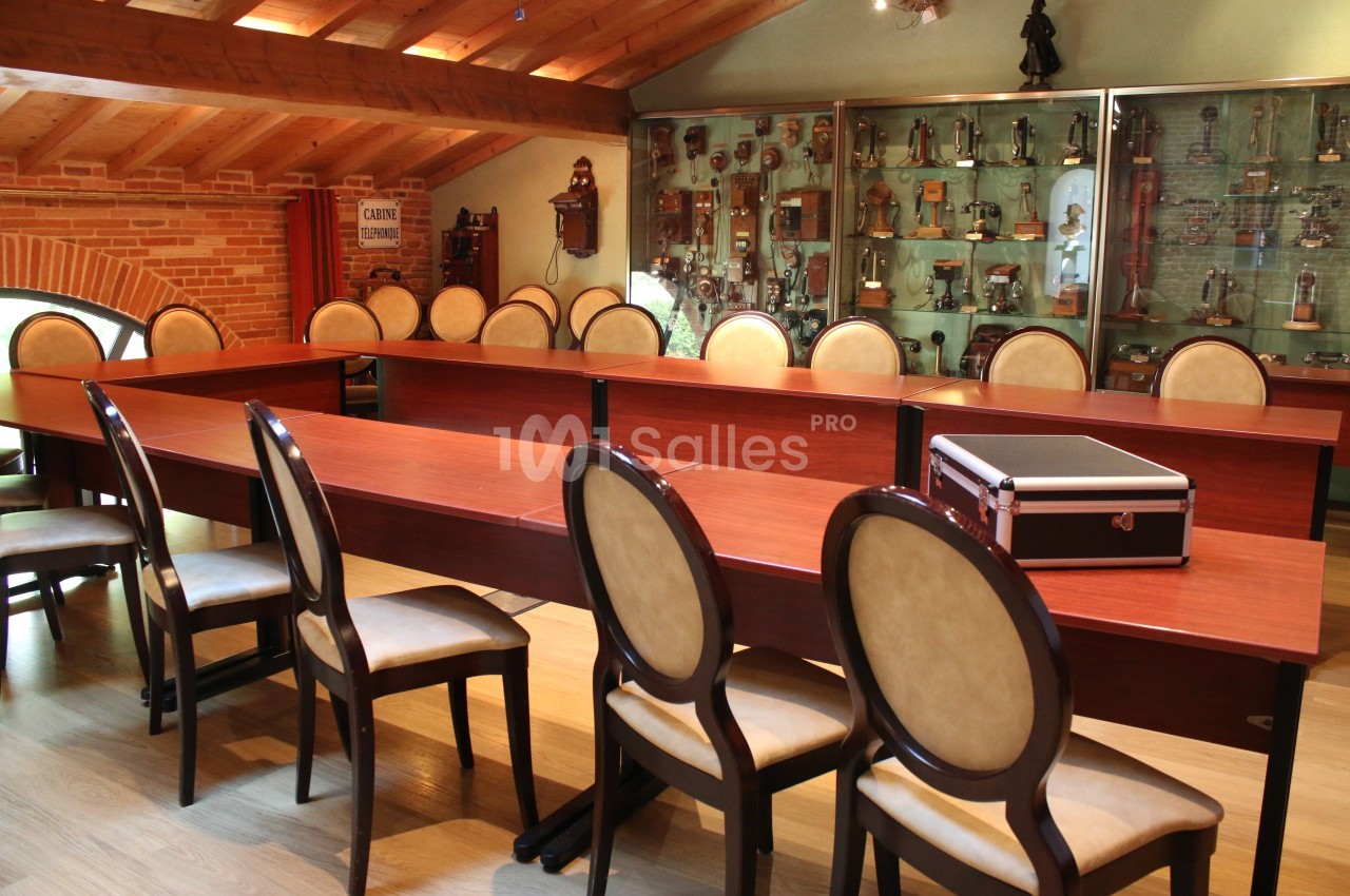 Salle de réunion avec des tables en bois disposées en U, des chaises rembourrées et une vitrine remplie de trophées.