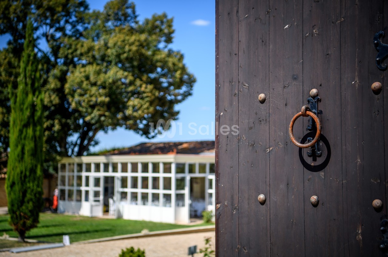 Porte en bois sombre avec anneau en métal au premier plan, jardin et bâtiment vitré en arrière-plan.