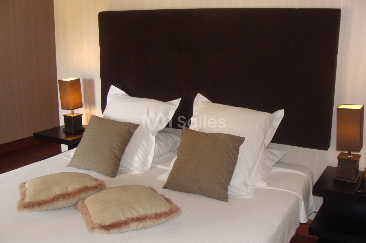 Lit double avec tête de lit sombre, draps blancs, coussins décoratifs et lampes de chevet allumées de chaque côté.