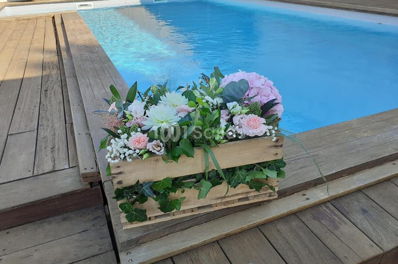 Arrangement floral dans une caisse en bois posé sur une terrasse en bois près d'une piscine.