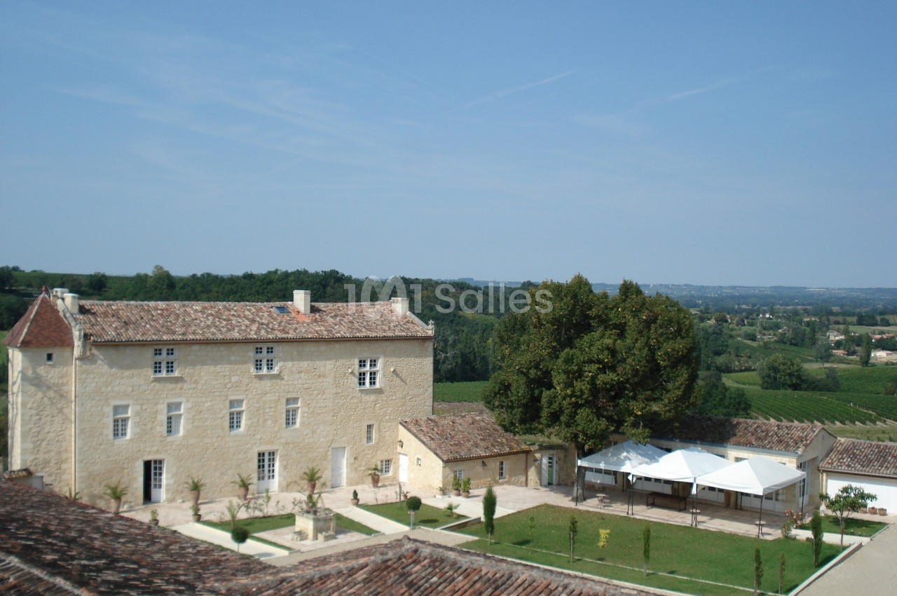 Vue d'un bâtiment en pierre entouré de jardins, avec des collines verdoyantes à l'arrière-plan.