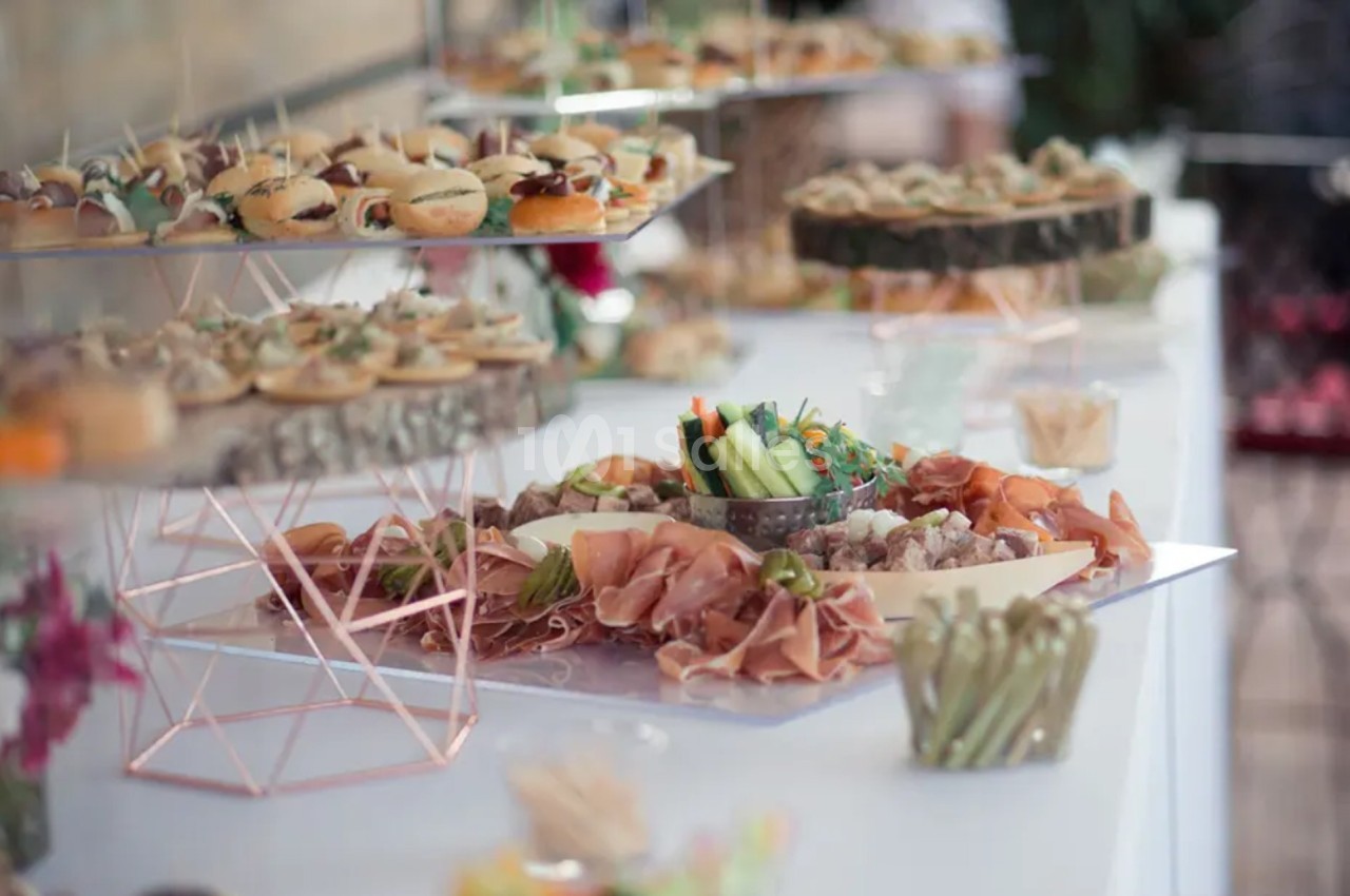 Buffet avec plateaux de charcuterie, légumes frais, mini-sandwichs et amuse-bouches sur une table décorée.