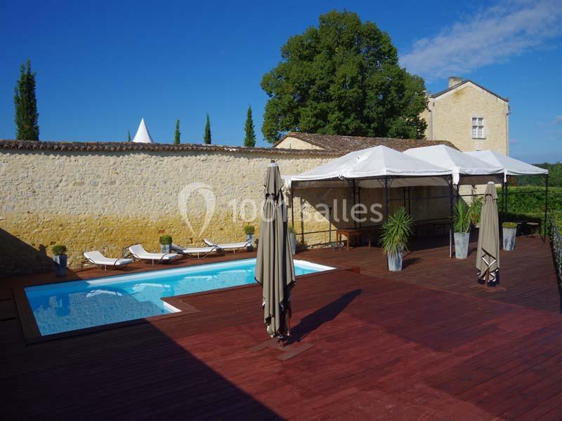 Terrasse en bois avec piscine, transats, parasols et tonnelles, entourée de murs en pierre et d'arbres.