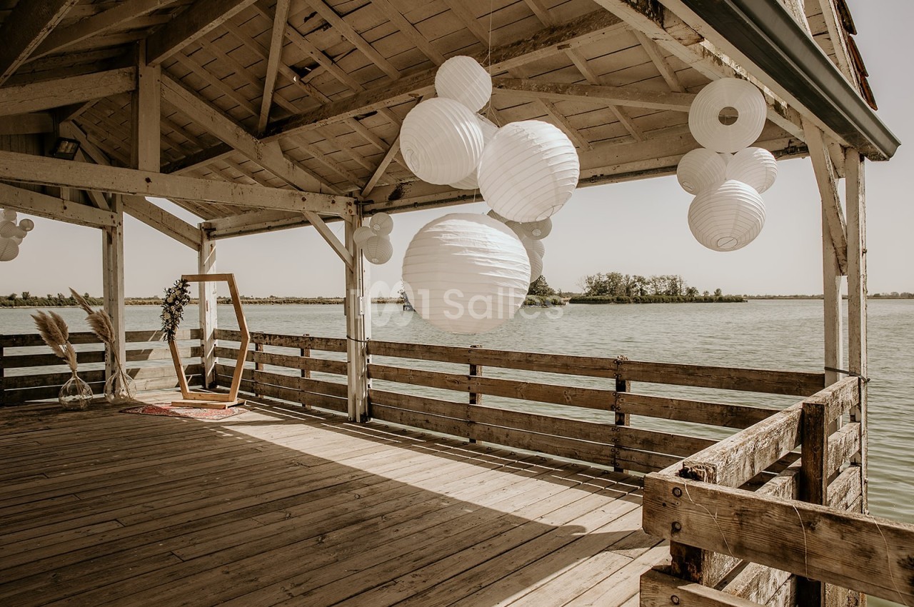 Terrasse en bois décorée de lanternes blanches suspendues, donnant sur un lac par une journée ensoleillée.