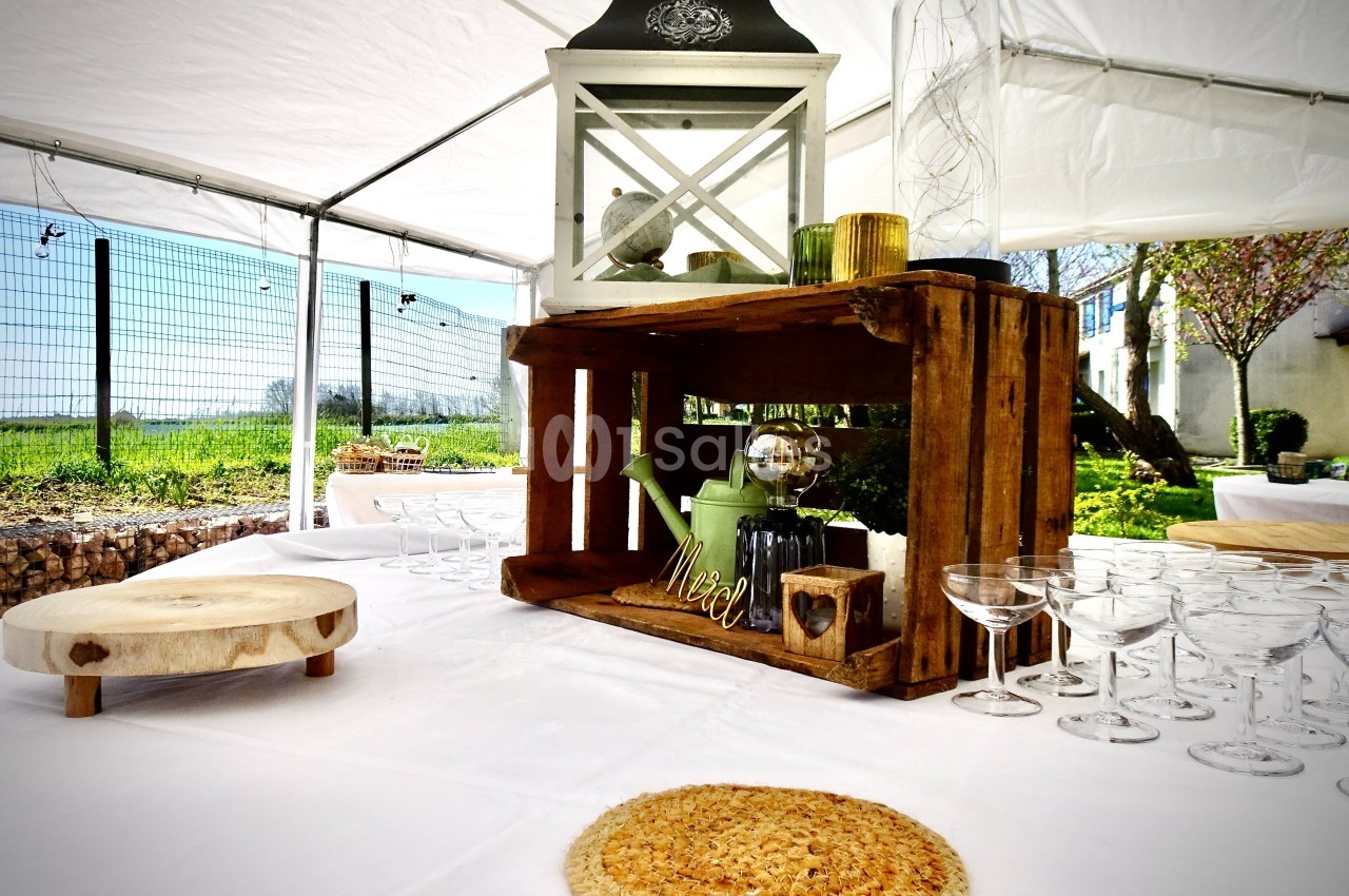 Table décorée sous une tente avec des caisses en bois, des verres, une lanterne et des éléments rustiques.