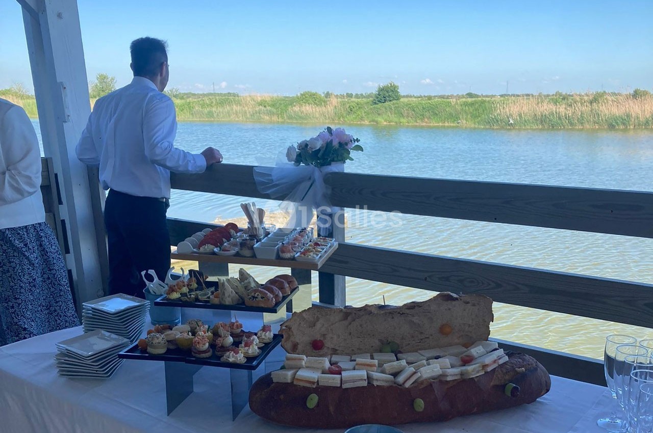 Buffet de nourriture variée disposé sur une table en extérieur, avec vue sur un plan d'eau et un homme de dos.