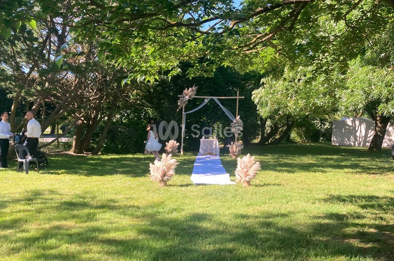 Allée décorée pour une cérémonie en plein air, avec arche florale et chaises sur une pelouse ombragée.