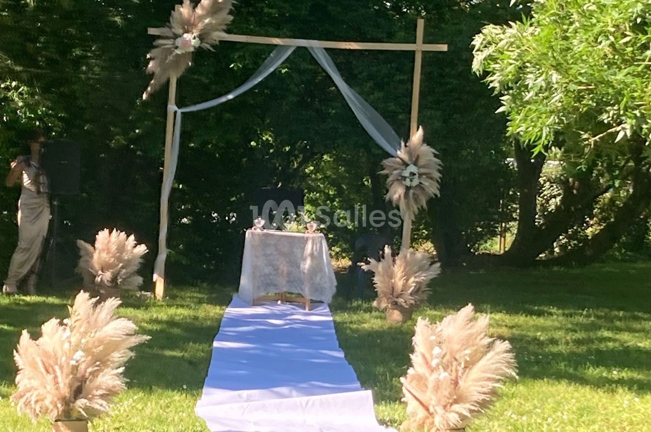 Arche de cérémonie en bois décorée de voilages et de fleurs séchées, installée sur une pelouse en plein air.