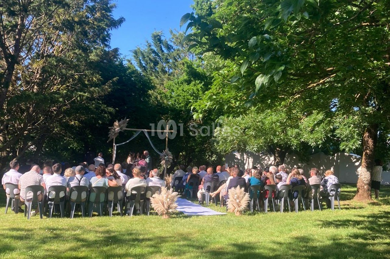 Groupe de personnes assises en extérieur lors d'une cérémonie sous un ciel dégagé, entourées d'arbres et de verdure.