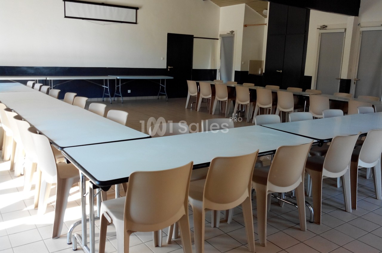 Salle lumineuse avec des tables blanches disposées en U et des chaises beiges, sol en carrelage clair.